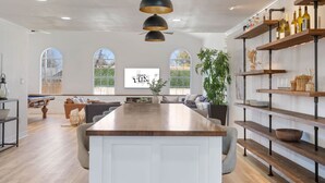 Una cocina amplia con una isla central, iluminación colgante y vistas al exterior a través de ventanas grandes.