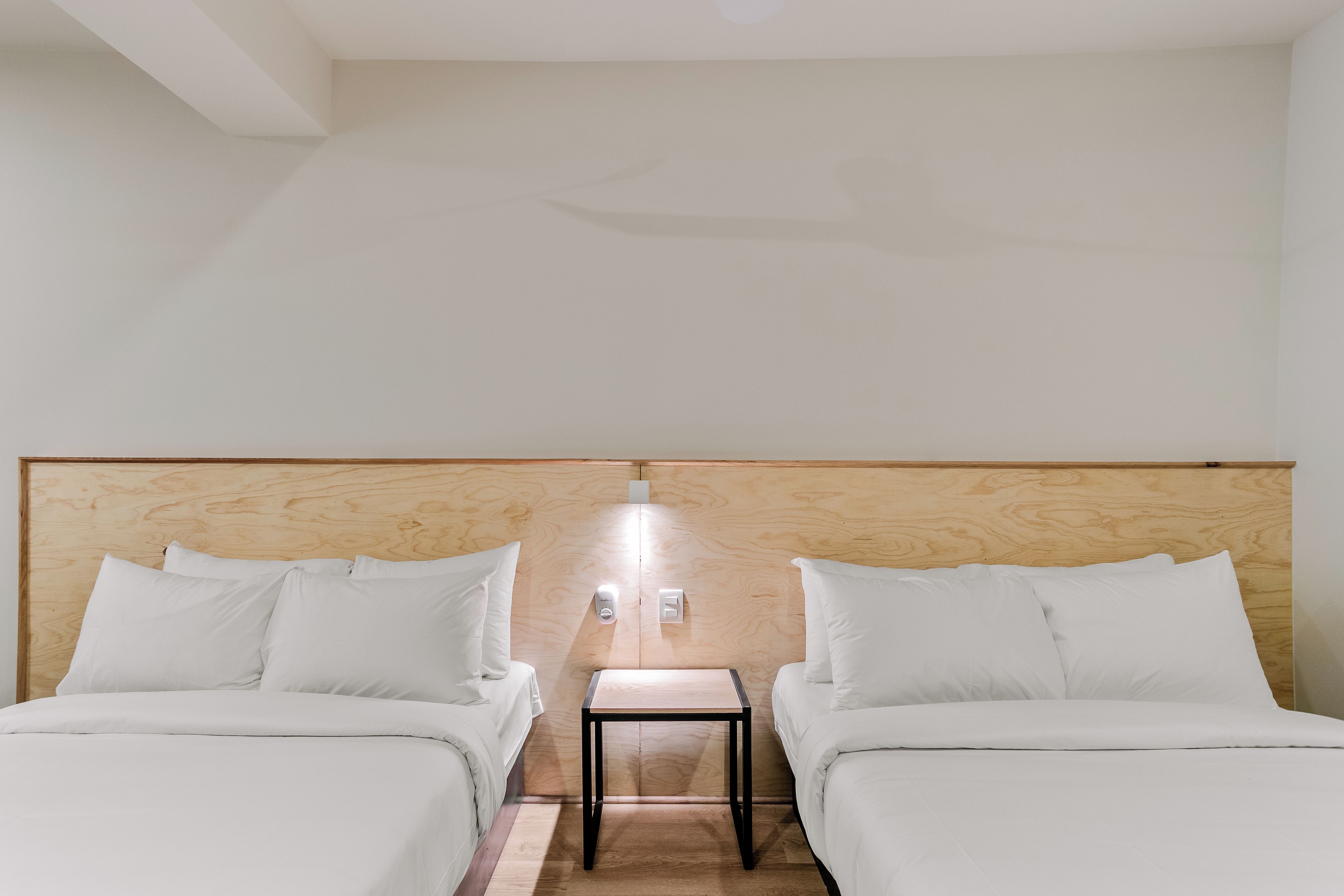 Une chambre d’hôtel avec deux lits, une petite table et une tête de lit en bois.