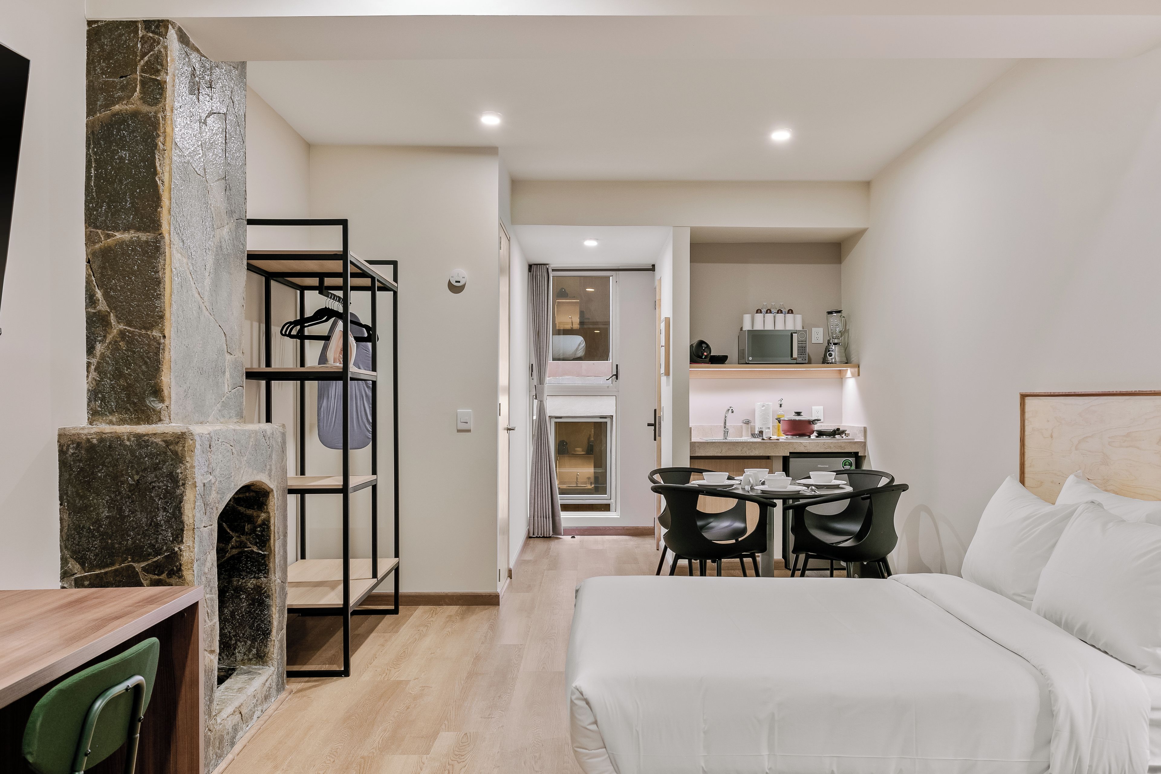 A modern bedroom with a bed, a desk, and a kitchenette.