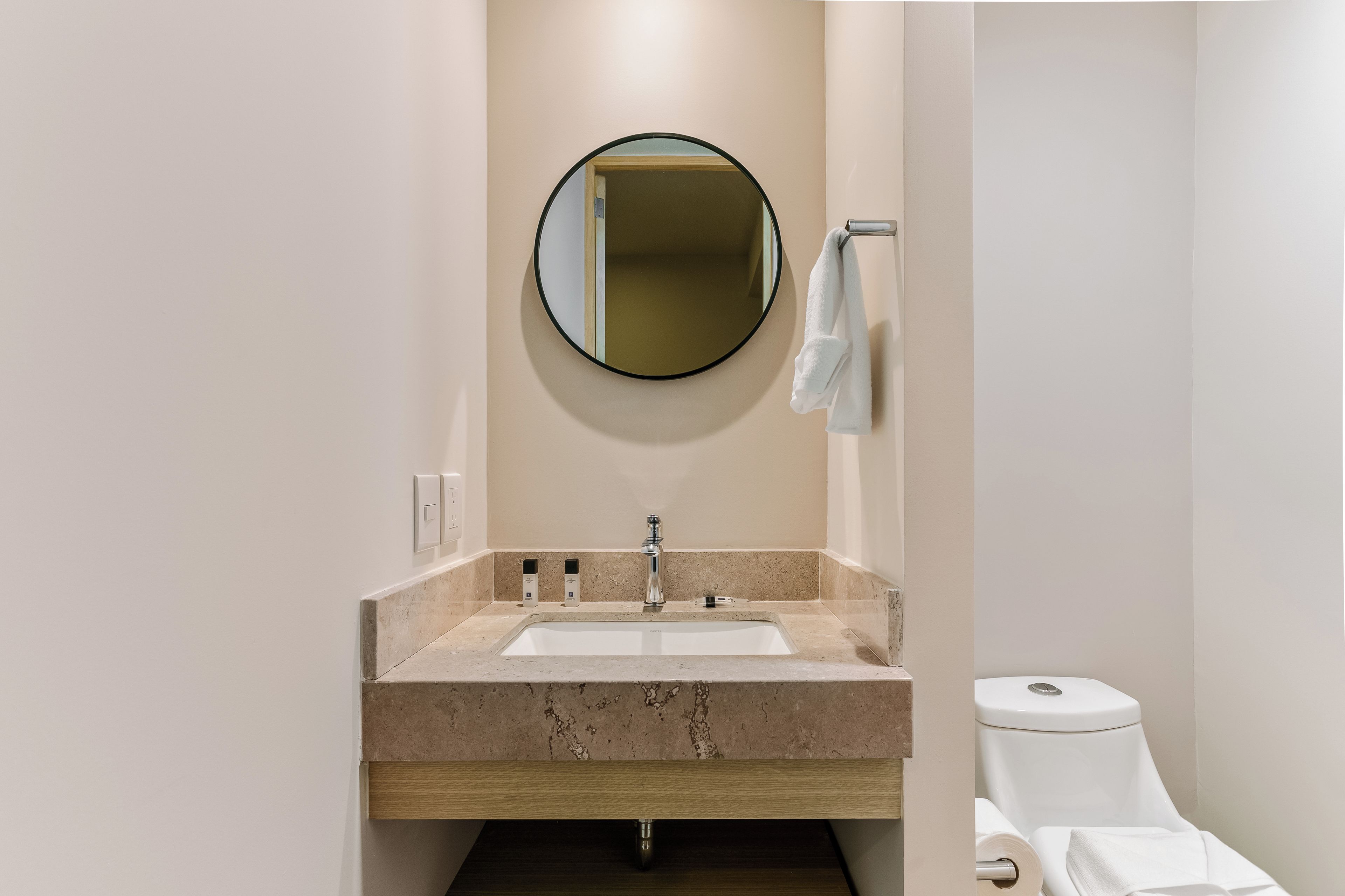 A bathroom with a marble sink, a round mirror, and a toilet.
