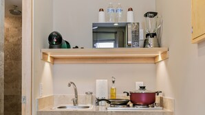Cocina compacta con lavamanos, estufa y microondas. Hay una repisa de madera sobre la estufa con varios utensilios de cocina.