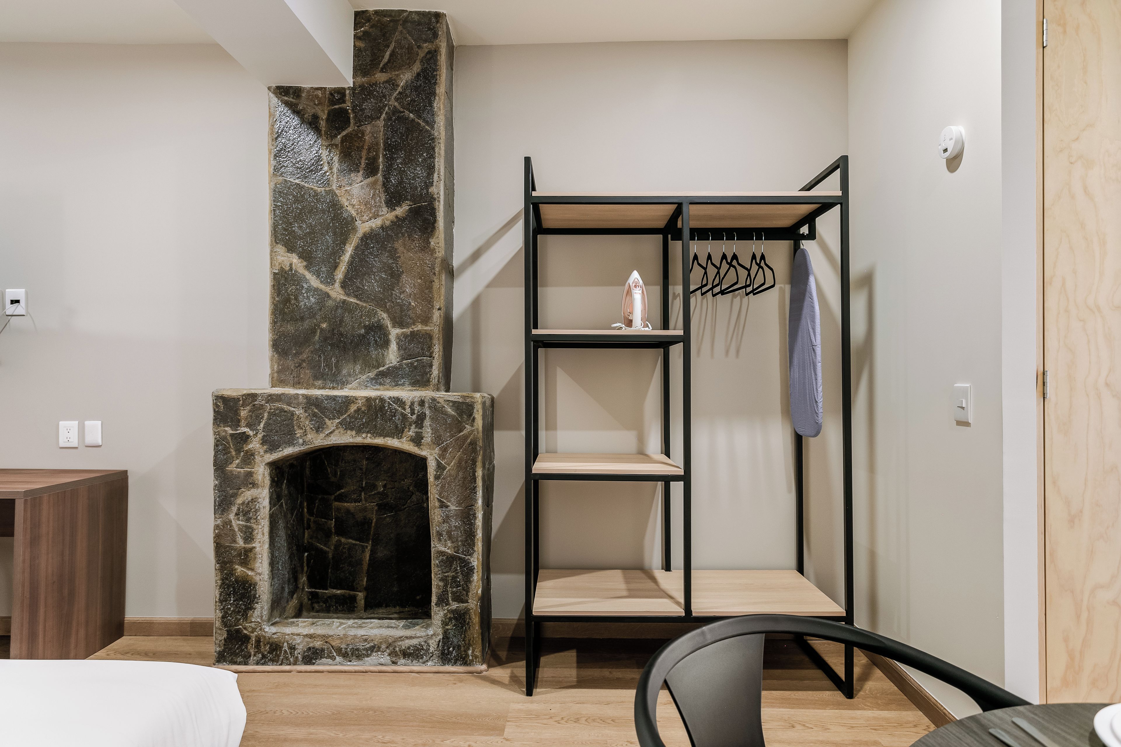 Une pièce avec une cheminée en pierre, une armoire en bois, une étagère en métal et une chaise.
