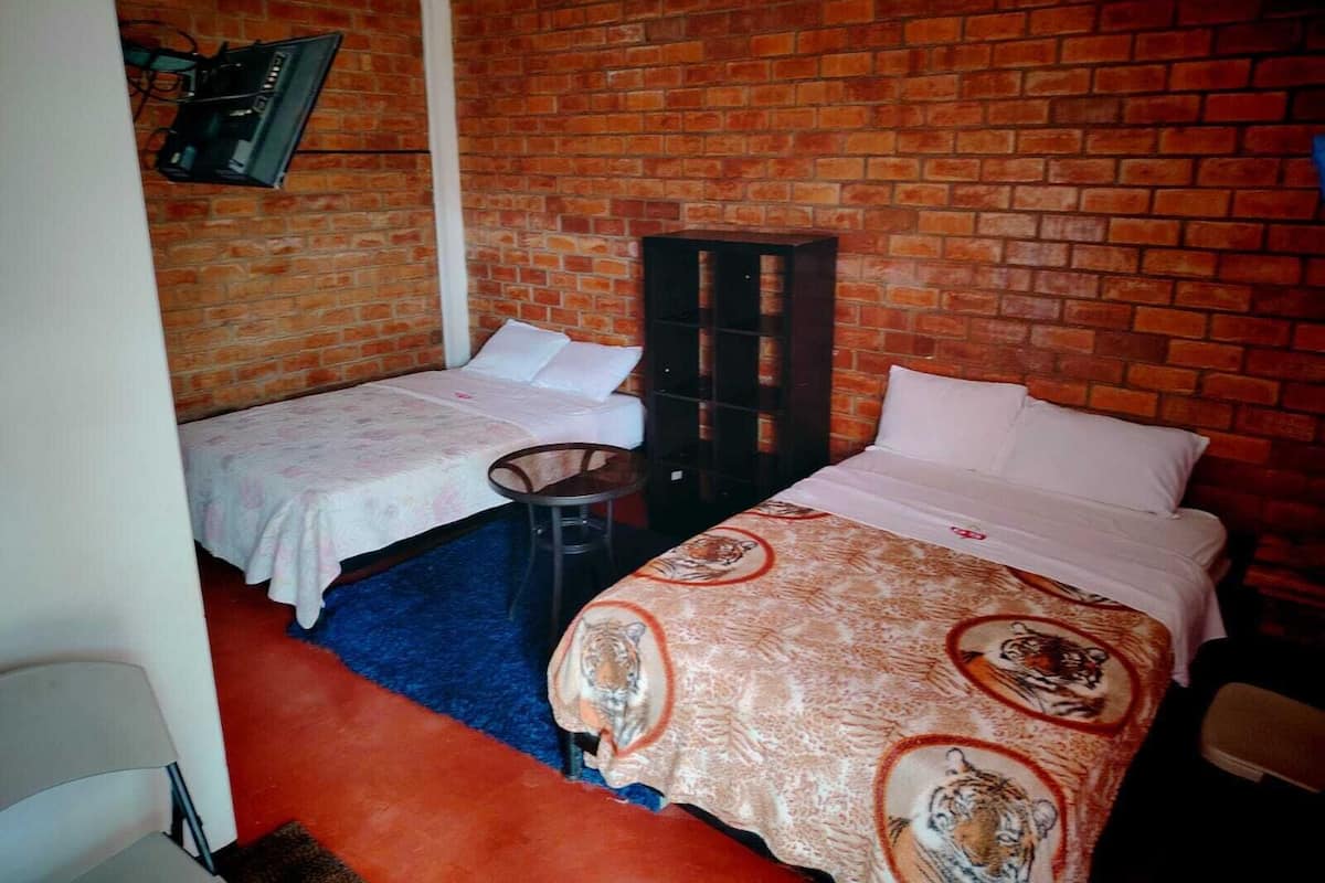 A room with two beds, a brick wall, and a small table.