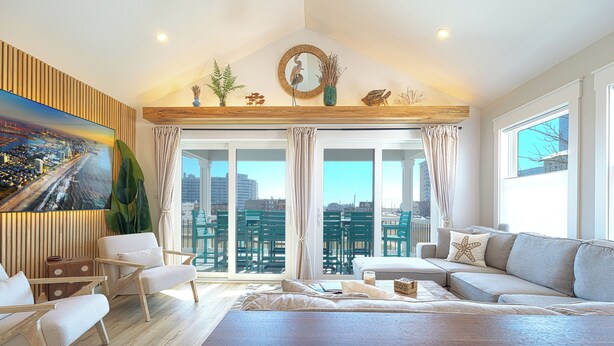 A spacious living room with a large window, a wooden ceiling, and a city view. - Designer Home • 1 Block to Boardwalk & Ocean • Stunning City & Ocean Views (Atlantic City)