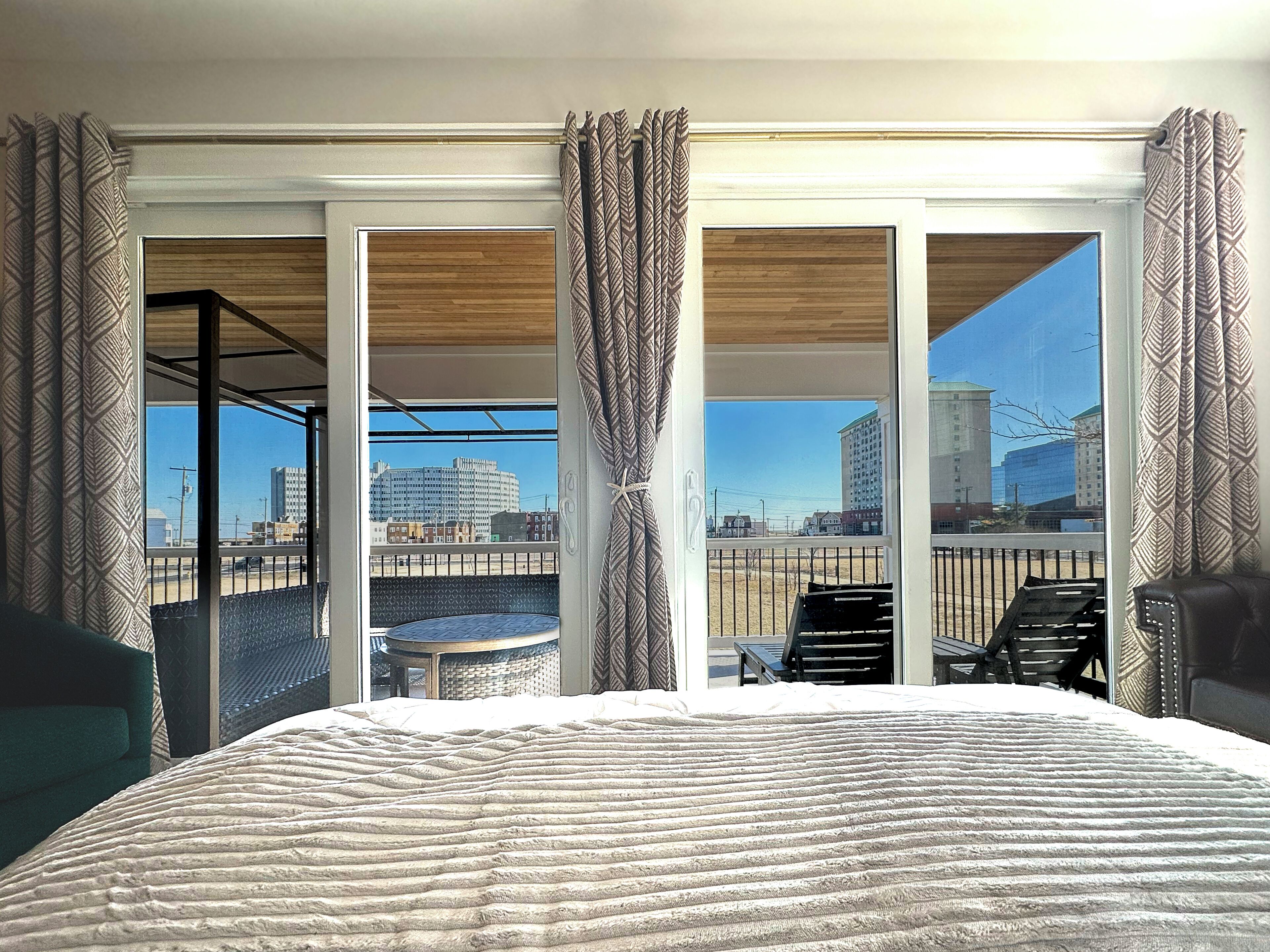 A hotel room with a large bed, a balcony with a view of the city, and a small table and chairs.