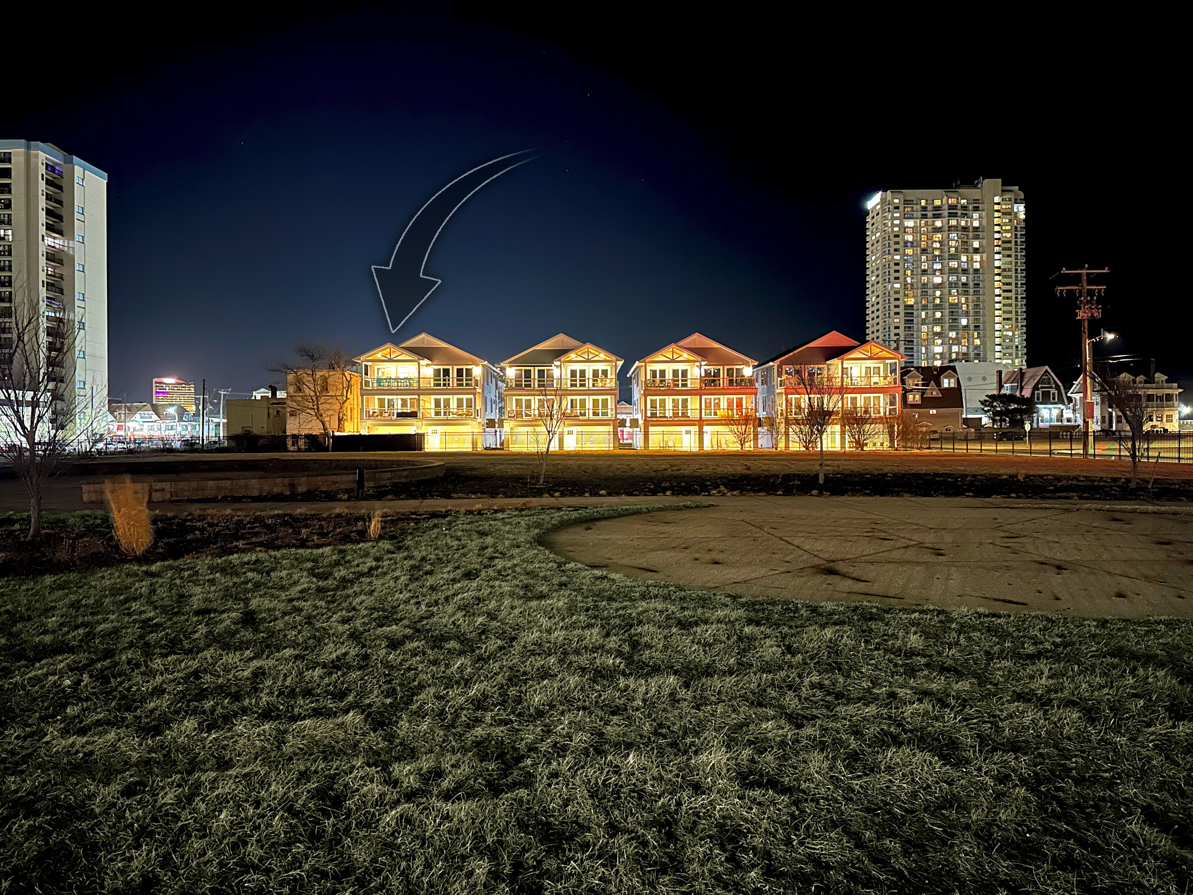A row of brightly lit, multi-story buildings with a clear view of the surrounding area, including a grassy field and a tall building in the background.