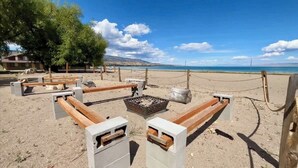 Area salotto sulla spiaggia con panche in cemento e un braciere, delimitata da una barriera in corda.