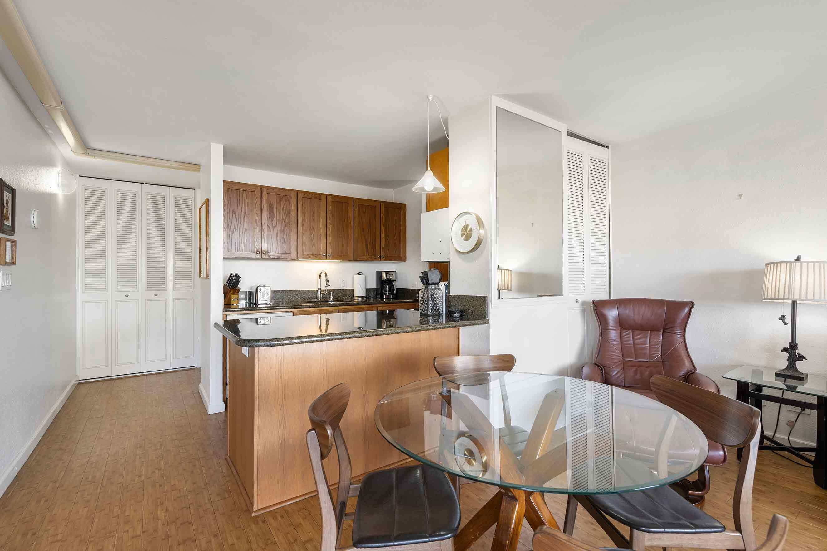 A compact kitchen with wooden cabinets, a glass dining table, and a brown leather chair.