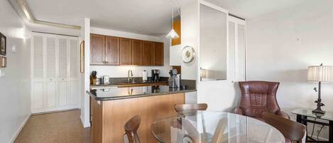 A compact kitchen with wooden cabinets, a glass dining table, and a brown leather chair.
