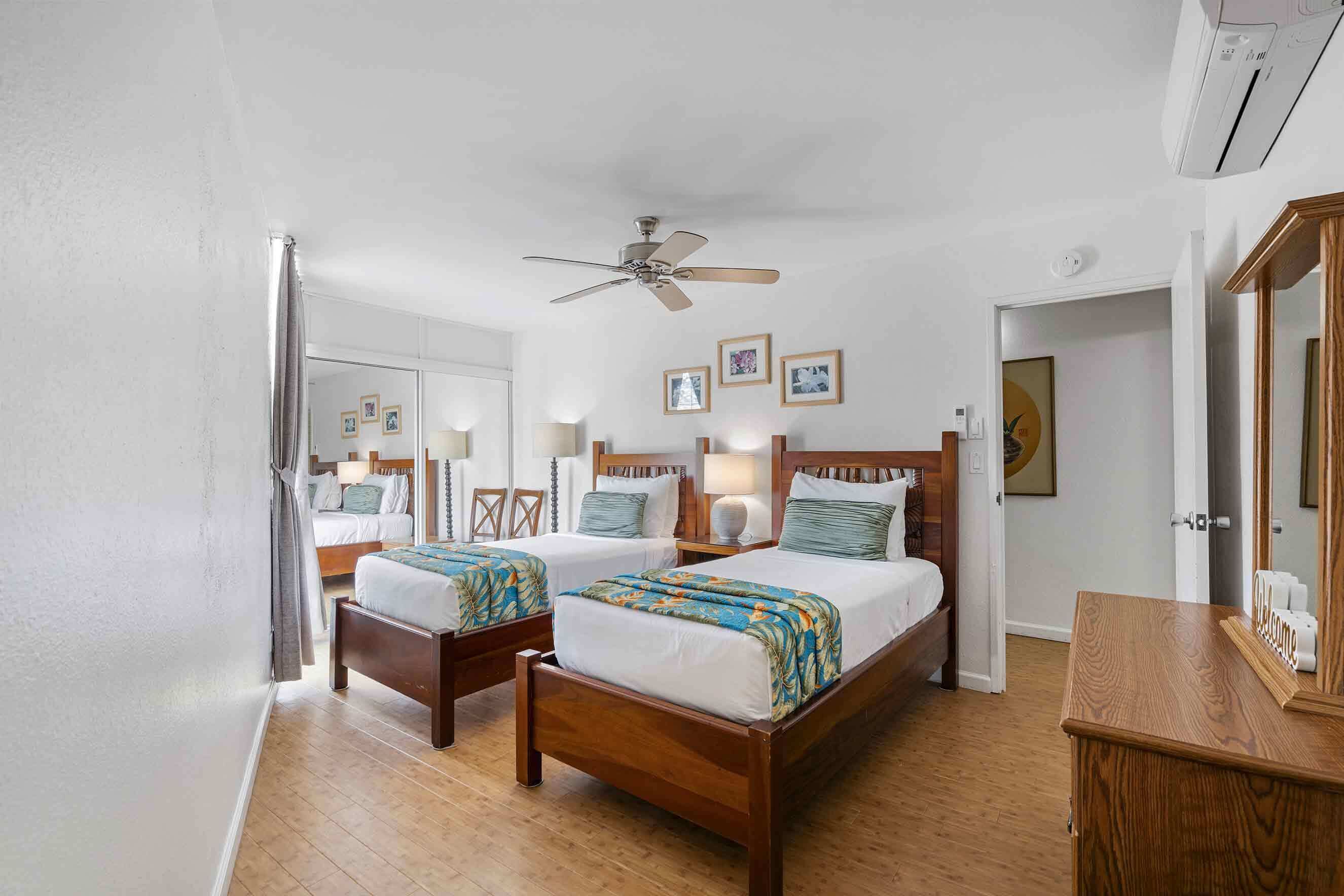 A hotel room with two wooden beds, a ceiling fan, and a wooden dresser.
