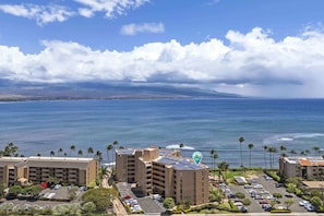 A coastal hotel with multiple floors, a parking lot, and a view of the ocean.