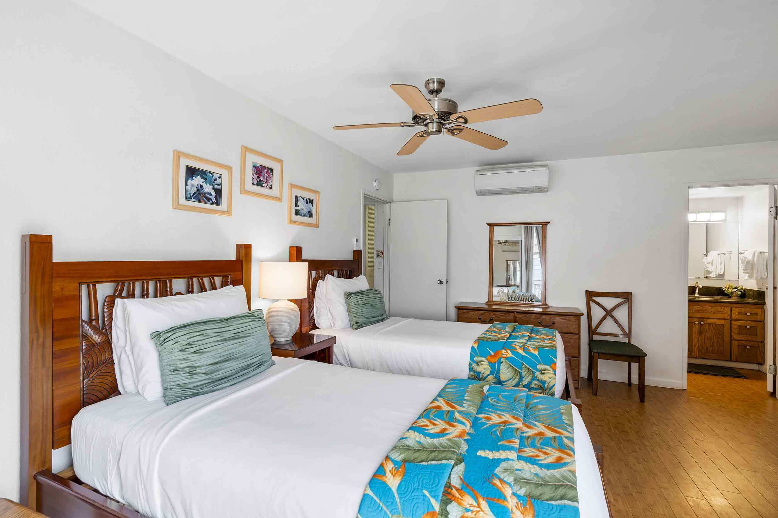 A hotel room with two beds, a ceiling fan, a mirror, a wooden dresser, and a bathroom visible through an open door.