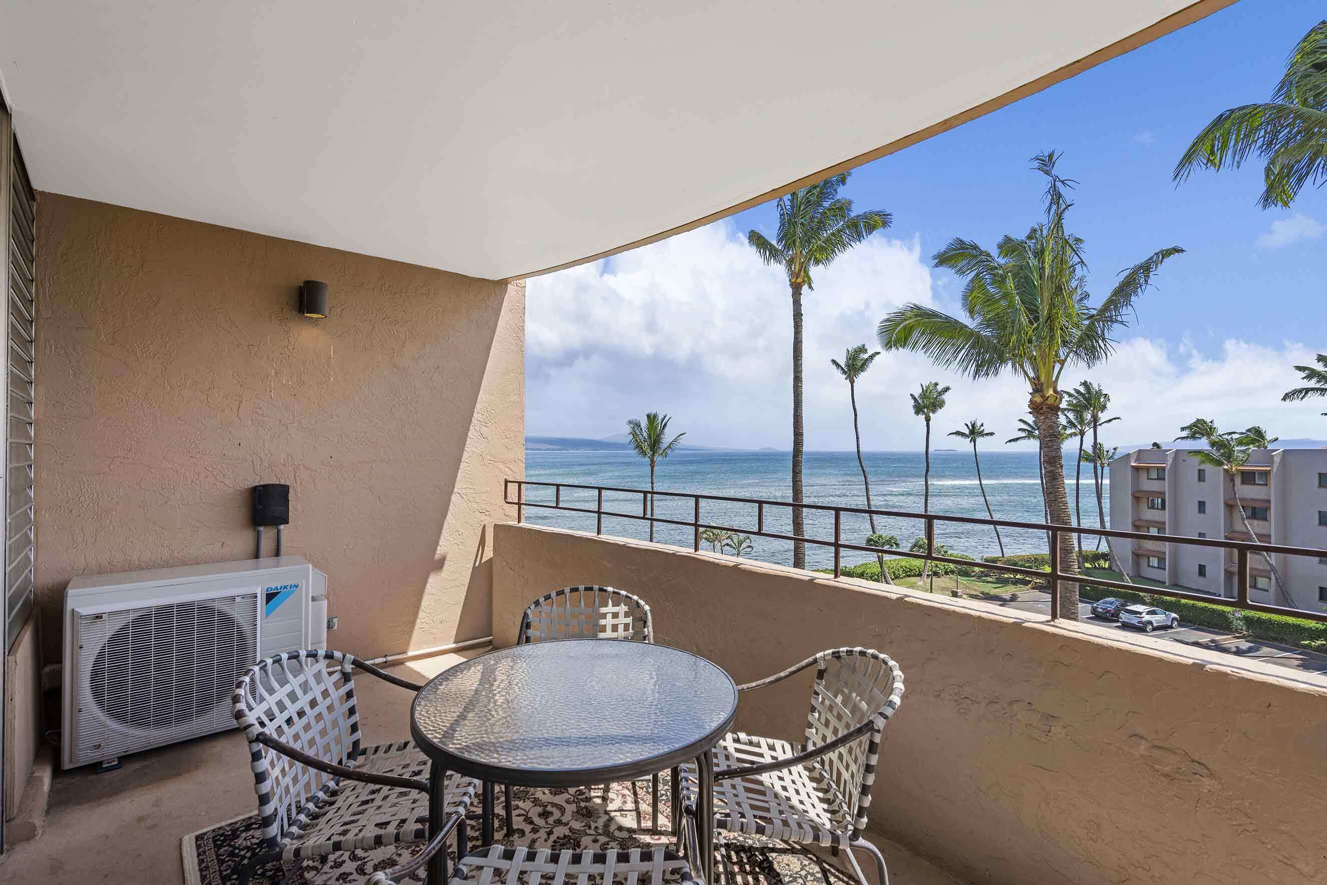 A balcony with a round table and chairs, overlooking a beach with palm trees and a view of the ocean.