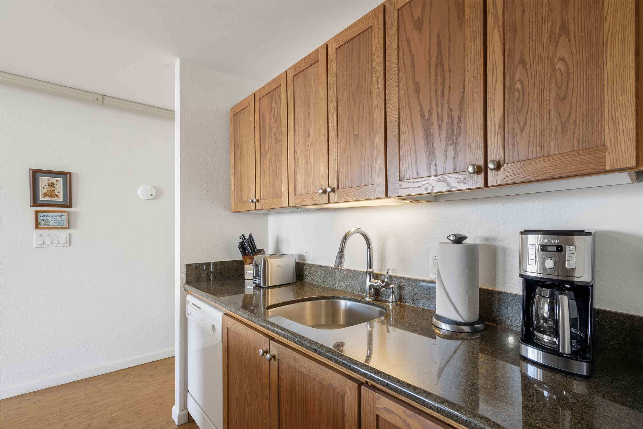 A kitchen with wooden cabinets, a stainless steel sink, a coffee maker, and a toaster.