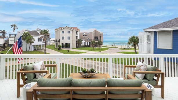 A balcony with wooden furniture and a view of a beach and ocean.