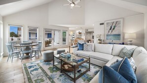 A spacious living room with a white sofa, a glass coffee table, and a dining area with blue chairs.