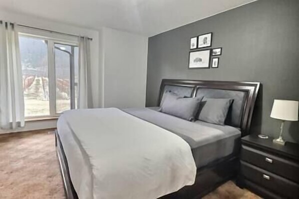 Un dormitorio con cama, mesita de noche, lámpara y ventana con cortinas.