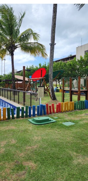 Children can play on the swing and climbing frame in this outdoor play area surrounded by a fence and a small pool.