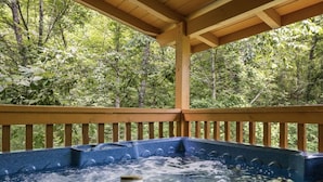 A hot tub under a wooden deck with a forest backdrop.