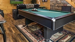 A cozy room with a pool table, a comfortable sofa, and a staircase leading to an upper level.