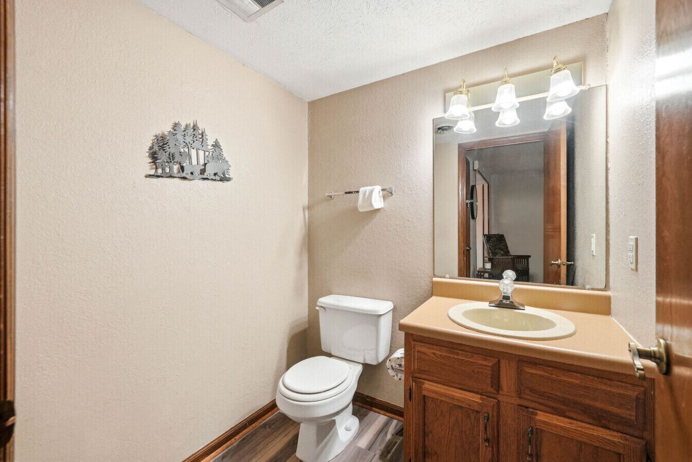 A bathroom with a toilet, sink, mirror, and a small decorative tree on the wall.