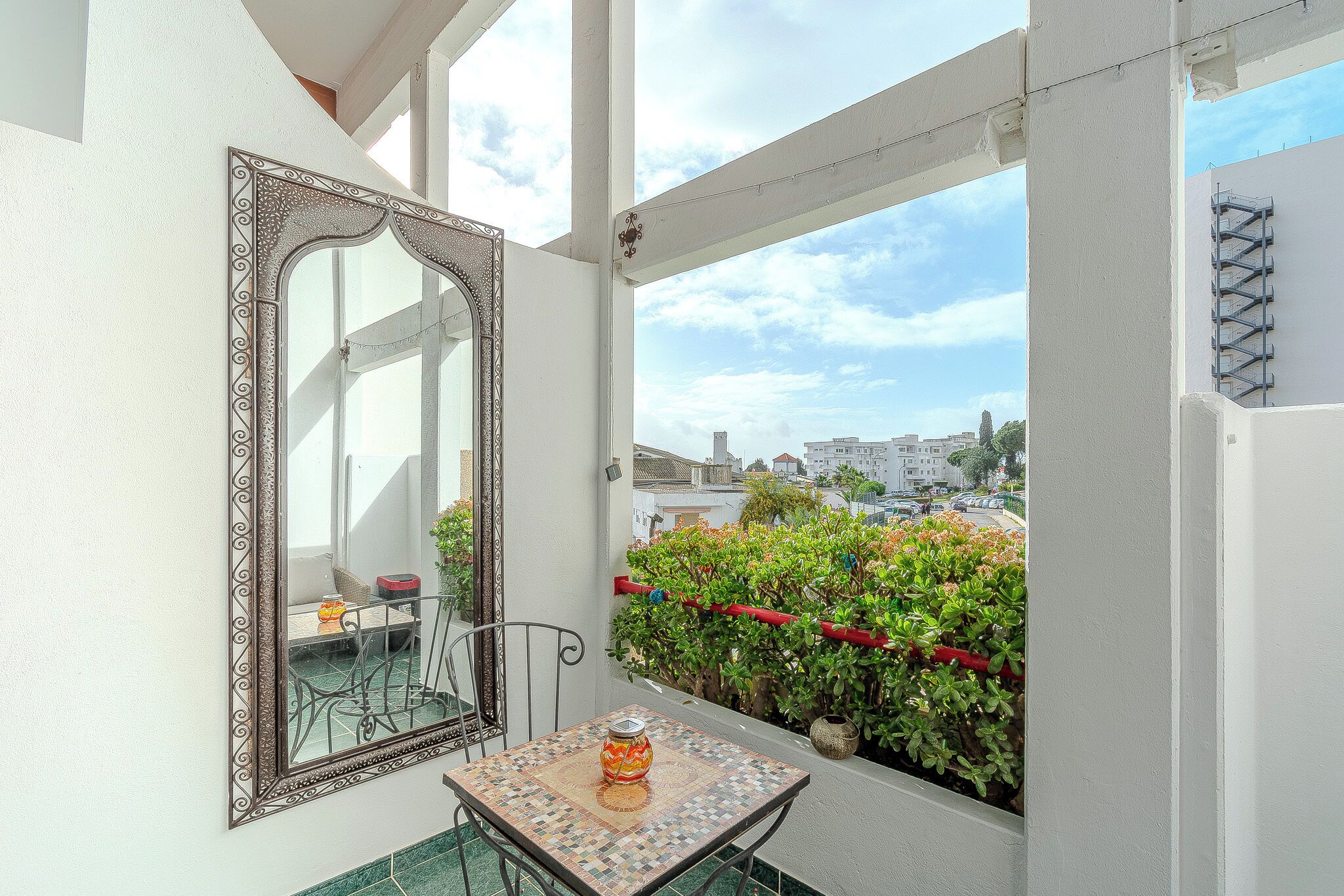 Ein Balkon mit Tisch, Stuhl, dekorativem Spiegel und Topfpflanzen.