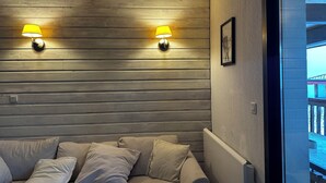 A room with a wooden headboard, two wall-mounted lamps, a framed picture, and a view of a balcony. - Font-Romeu: large T4 in residence with magnificent view of valley and mountains (Font-Romeu-Odeillo-Via)