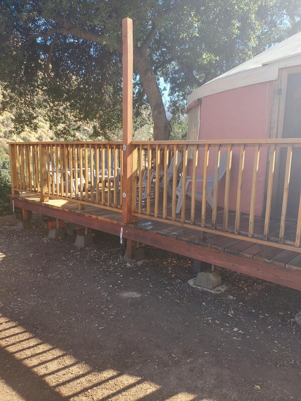 Une terrasse en bois avec des chaises, un petit bâtiment et un arbre en arrière-plan.