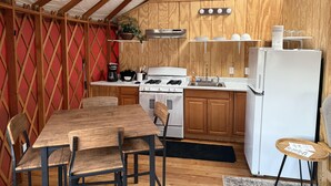 A compact kitchen with wooden cabinets, a gas stove, a white refrigerator, and a dining area with a wooden table and chairs. - Yurt - Beautiful One-Bedroom Yurt (Winters)