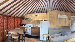 A compact kitchen with a stove, sink, and refrigerator, a wooden dining table with chairs, and a grey sofa. - Yurt - Beautiful One-Bedroom Yurt (Winters)