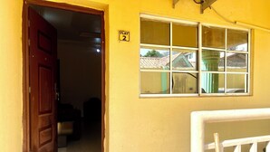 A yellow building with a wooden door, a window, and a tiled floor.