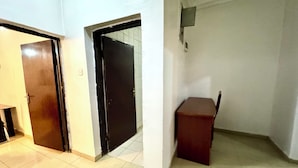 A hallway with two doors, one open and one closed, leading to a room with a small table and a chair.