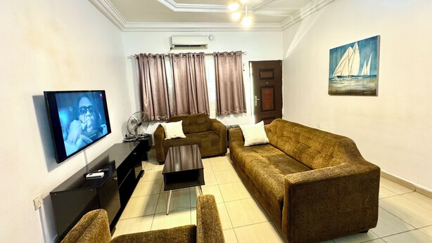 A living room with a sofa set, a TV, a fan, and a painting on the wall.