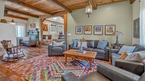 A spacious living room with wooden beams, a colorful rug, and multiple seating areas.