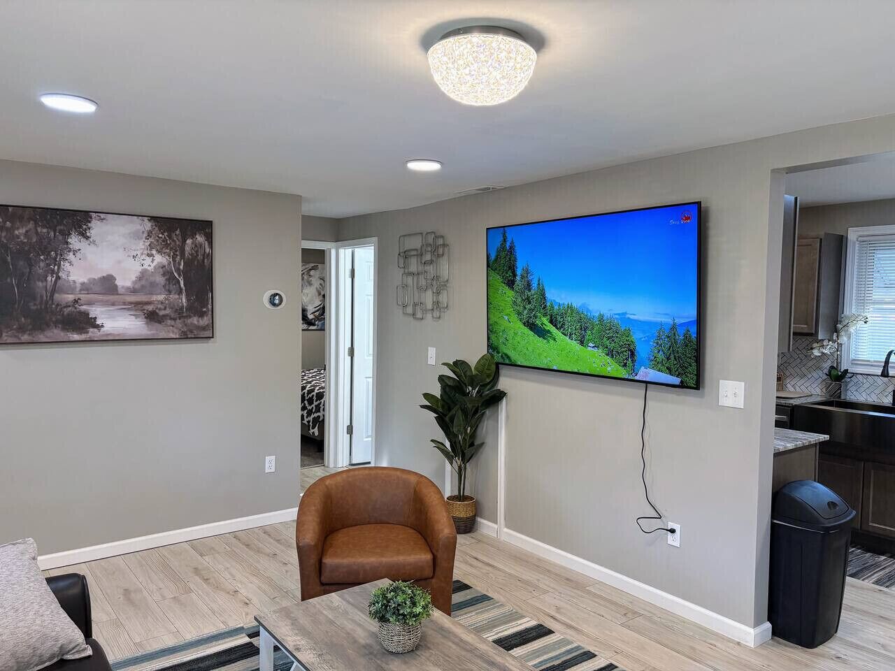 A modern living room with a flat-screen TV, a brown leather chair, a potted plant, and a painting on the wall.