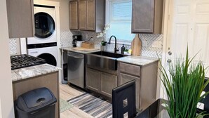 Una cocina compacta con lavadora y secadora integradas, electrodomésticos de acero inoxidable y un salpicadero de azulejos en patrón de espiga.