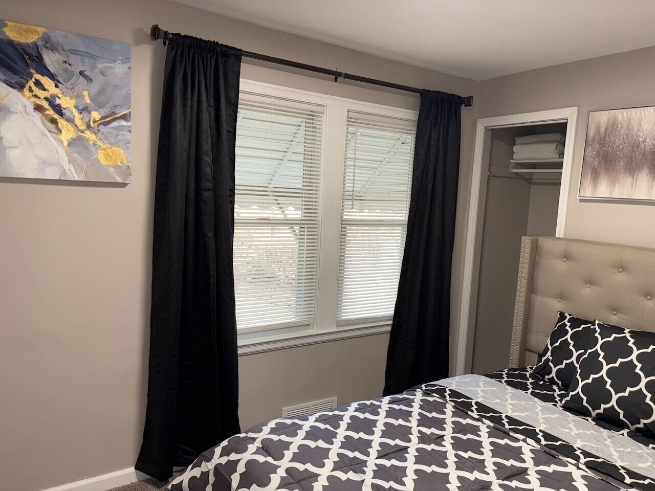 Une chambre à coucher avec un lit, une fenêtre avec des stores, une porte et un tableau au mur.