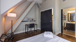Ein Schlafzimmer mit einem Bett, einem Schreibtisch, einem Stuhl, einer Lampe und einer Treppe.