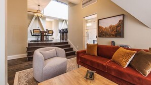 Ein geräumiges Wohnzimmer mit einem roten Sofa, einem grauen Sessel und einem Holztisch. Eine Treppe führt zu einem Essbereich mit einer Deckenleuchte.