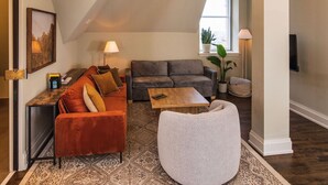 Ein geräumiges Loft mit hohen Decken, einem großen Fenster und einer gemütlichen Sitzecke mit Sofa und Hocker.