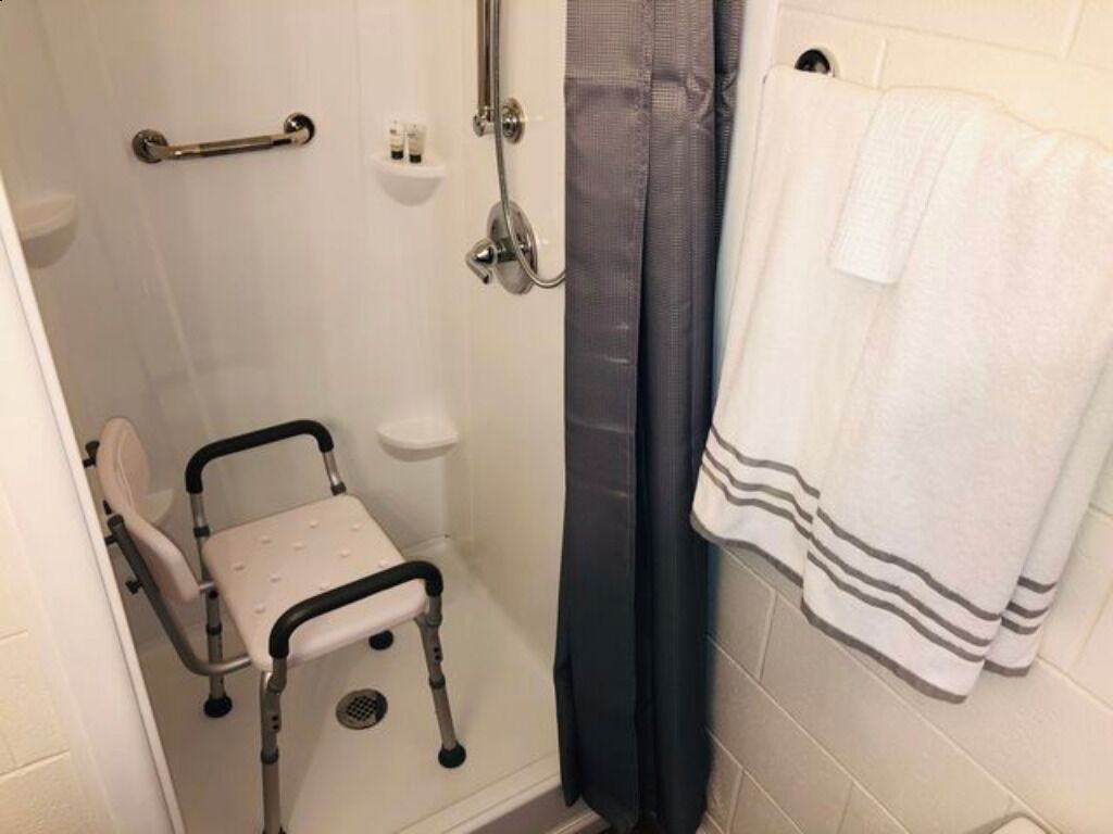 A bathroom with a shower, a grab bar, a wheelchair, and a towel rack.