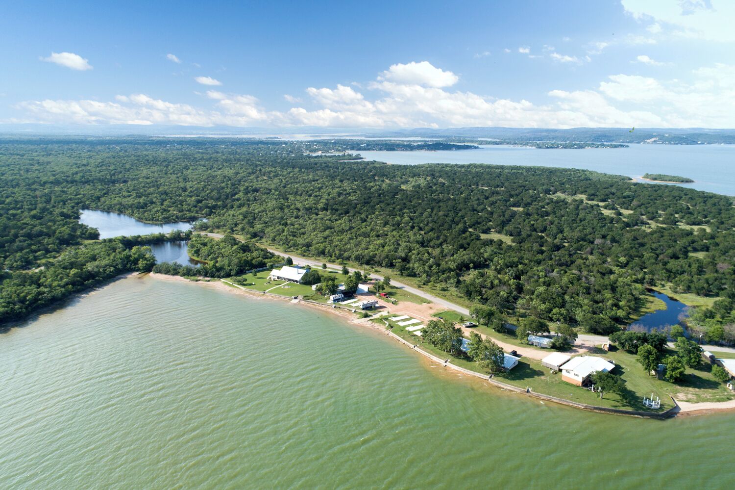 An aerial view of a lakeside property with a small cluster of buildings, a dock, and a boat.