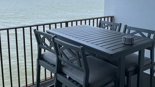 Een balkon met een tafel en stoelen, met uitzicht op een wateroppervlak.