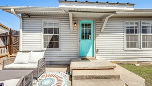 Een huis met een turquoise voordeur, een veranda met rieten meubilair, en een betonnen trap naar de deur.