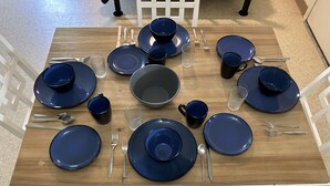 A dining table set with blue plates, bowls, and cups, surrounded by white chairs. - The Lakeside Studio 6 (Bluffton)