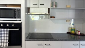 A kitchen with white cabinets, a microwave, an oven, a gas stove, and a shelf with books and kitchen items.