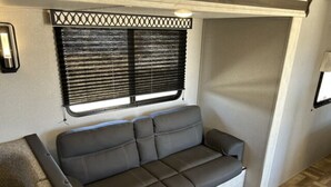 Interior compacto de una autocaravana con sofá, ventana con persianas y una pequeña mesa.