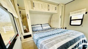 Dormitorio compacto de una caravana, con cama, ventana y una pequeña zona de kitchenette.