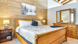 Camera da letto con rivestimento in legno, un letto, lampade sui comodini, una cassettiera e uno specchio.