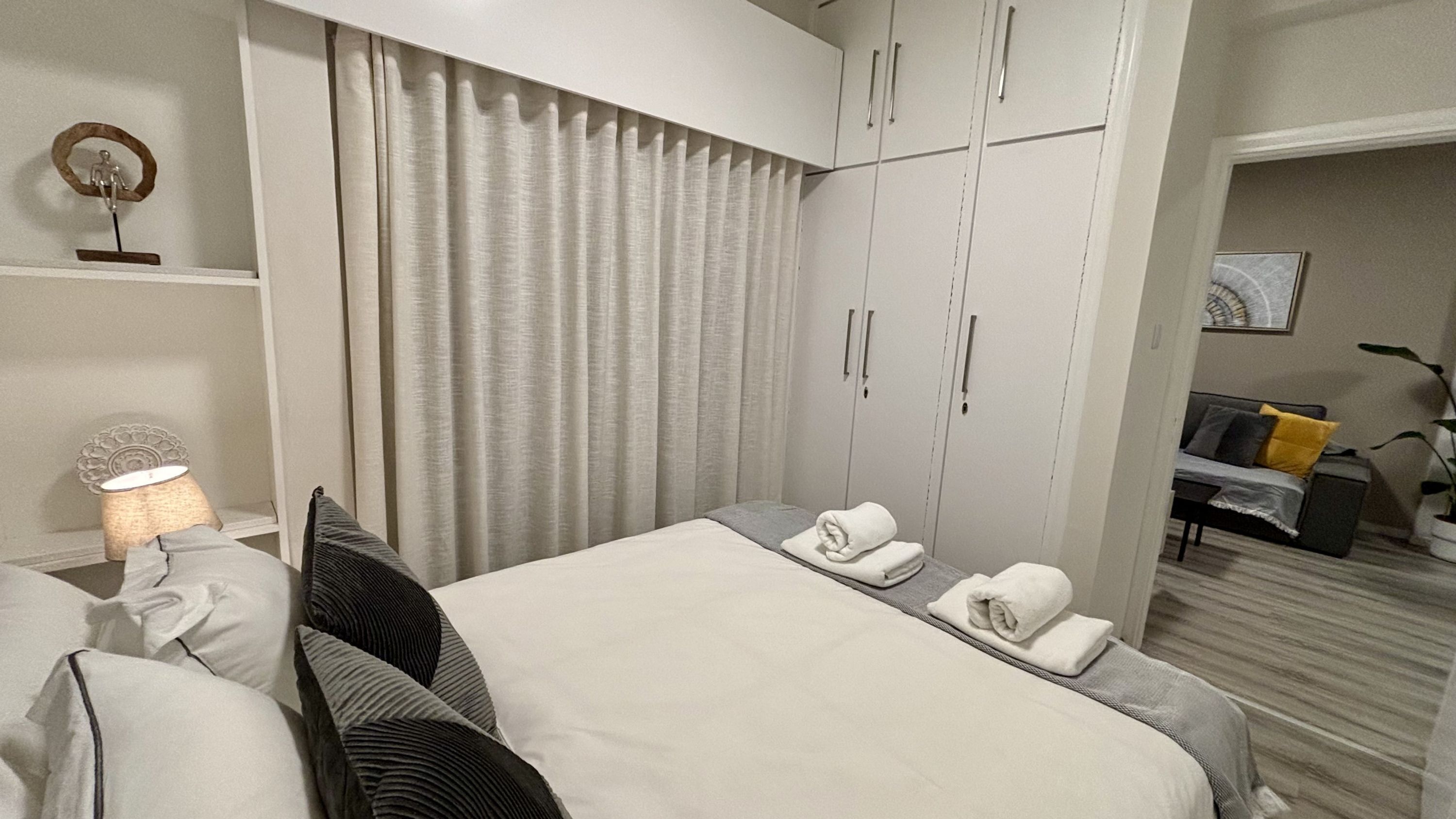 Habitació d'hotel amb un llit, almoines, una làmpada, un armari i un sofà al fons.